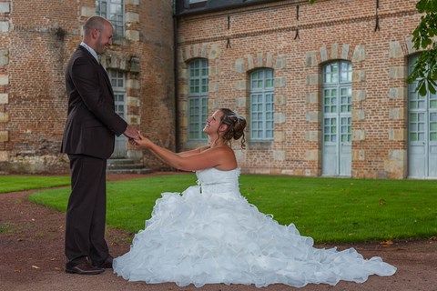 La mariée à genoux prend les mains de son mari